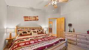 A bedroom with a wooden bed, a wooden dresser, a ceiling fan, and a wall-mounted tapestry. - Pine Cottage (Big Bear Lake)