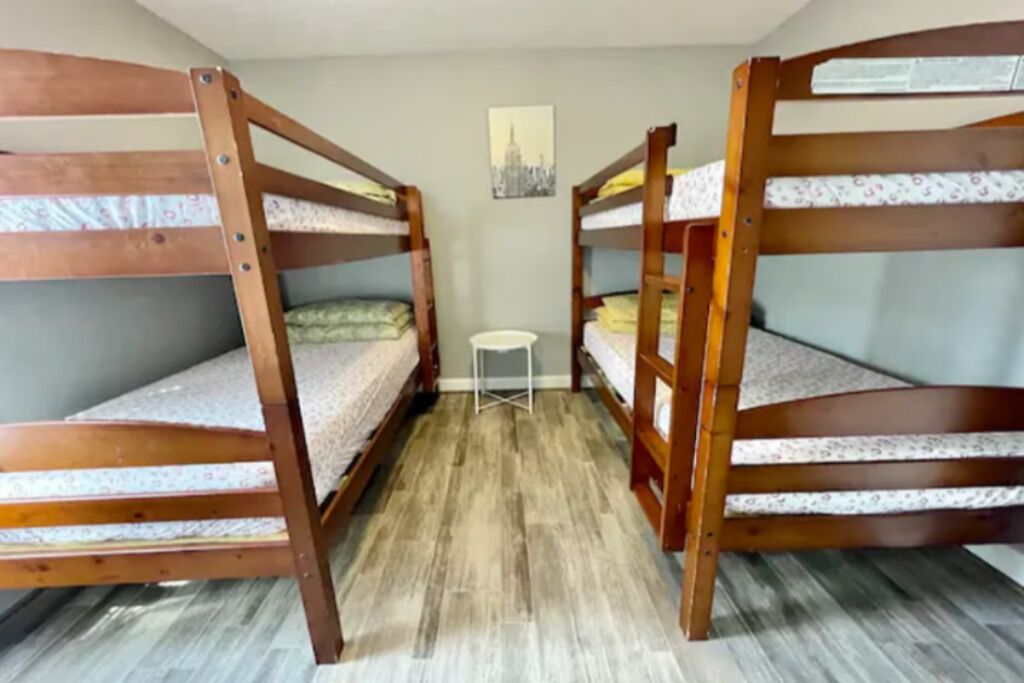 A room with three bunk beds, a small white chair, and a cityscape painting on the wall.