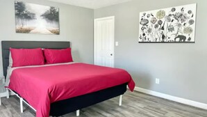 Un dormitorio con cama, una puerta y dos cuadros en la pared.