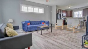 Una sala de estar con sofá, mesa de centro y sillones, además de una cocina con alacenas y electrodomésticos, y un ventilador de techo.