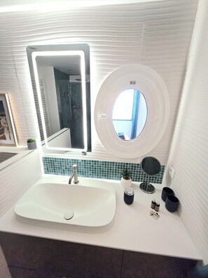 A bathroom with a white sink, a large mirror, a round mirror, and a potted plant. - Air-conditioned apartment, fantastic sea view, tramway and amenities nearby (Nice)