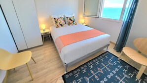Ein Hotelzimmer mit einem Bett, zwei Nachttischen, einem Sessel, einem Fenster mit Blick und einem gemusterten Teppich.