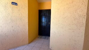 A narrow hallway with a textured wall, a black door with a decorative design, and a welcome mat at the entrance. - Gorgeous Third-Level Condo Princesa D-308 (Puerto Peñasco)