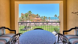 Un balcon avec une table et des chaises, donnant sur une plage et des palmiers.