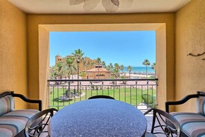 A balcony with a table and chairs, overlooking a beach and palm trees. - Stunning Views in 2nd Level Condo Princesa B-203 (Puerto Peñasco)