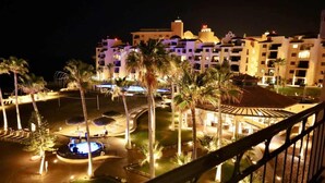 A hotel with multiple floors, a swimming pool, and palm trees. - Ground Level Condo near Pool Princesa B-101 (Puerto Peñasco)