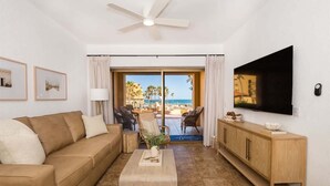 A living room with a sofa, coffee table, and TV, a wooden cabinet, and a view of the beach. - Ground Level Condo near Pool Princesa B-101 (Puerto Peñasco)