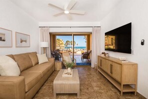 A living room with a sofa, coffee table, and TV, a wooden cabinet, and a view of the beach. - Ground Level Condo near Pool Princesa B-101 (Puerto Peñasco)