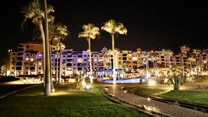 A hotel with multiple floors, a swimming pool, and palm trees. - Ground Level Condo near Pool Princesa B-101 (Puerto Peñasco)