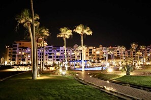 A hotel with multiple floors, a swimming pool, and palm trees. - Ground Level Condo near Pool Princesa B-101 (Puerto Peñasco)