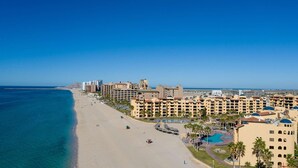 A coastal hotel with multiple buildings, a beach, and a clear blue sky. - Ground Level Condo near Pool Princesa B-101 (Puerto Peñasco)
