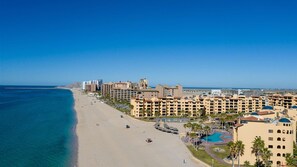 A coastal hotel with multiple buildings, a beach, and a clear blue sky. - Ground Level Condo near Pool Princesa B-101 (Puerto Peñasco)