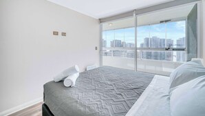 Een moderne slaapkamer met een groot bed, uitzicht op de stad via een schuifdeur, en een stadsbeeld te zien door het raam.