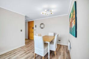 Ein Essbereich mit Holztisch und weißen Stühlen, einer Deckenleuchte und einem Gemälde an der Wand.