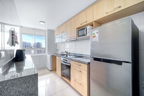 A modern kitchen with stainless steel appliances, wooden cabinets, and a large window offering a city view.