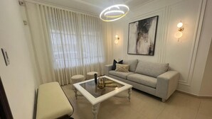 Una sala de estar con una mesa de centro de vidrio, un sofá, un banco y un cuadro en la pared.
