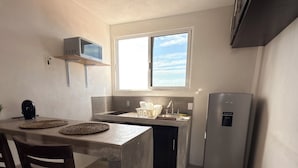 Cocina compacta con microondas integrado, refrigerador y ventana sobre el lavamanos.