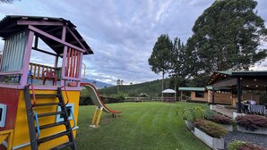 A playground with a slide and climbing area, surrounded by well-maintained grass and trees.
