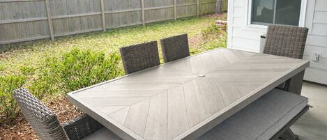 A rectangular outdoor dining table with a herringbone pattern, surrounded by wicker chairs with cushioned seats.