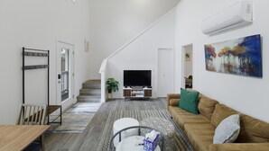 A modern living room with a staircase, a flat-screen TV, a sofa, and a painting on the wall. - Peaceful Central District Retreat 3 bdrm, patio (Seattle)