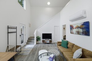 Ein modernes Wohnzimmer mit Treppe, einem Flachbildfernseher, einer Couch und einem Gemälde an der Wand.