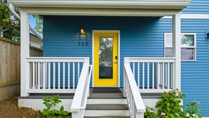 A blue house with a yellow door, white railings, and a number '125' on the wall. - Peaceful Central District Retreat 3 bdrm, patio (Seattle)