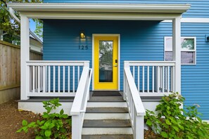 Ein blaues Haus mit gelbem Eingangsbereich, weißen Geländern und der Hausnummer 125 an der Wand.