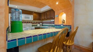 A kitchen with a tiled backsplash, wooden cabinets, and a water dispenser. - Charming Colorful Condo Near Pool - Pueblos D-101 (Puerto Peñasco)