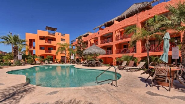 A hotel with a swimming pool, lounge chairs, and a thatched-roof building. - Charming Colorful Condo Near Pool - Pueblos D-101 (Puerto Peñasco)