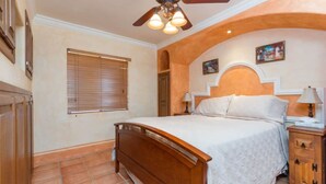 A bedroom with a wooden bed, a ceiling fan, a nightstand, and a window with blinds. - Charming Colorful Condo Near Pool - Pueblos D-101 (Puerto Peñasco)