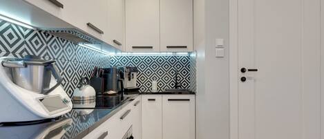 A compact kitchen with white cabinets, a black countertop, and patterned backsplash.