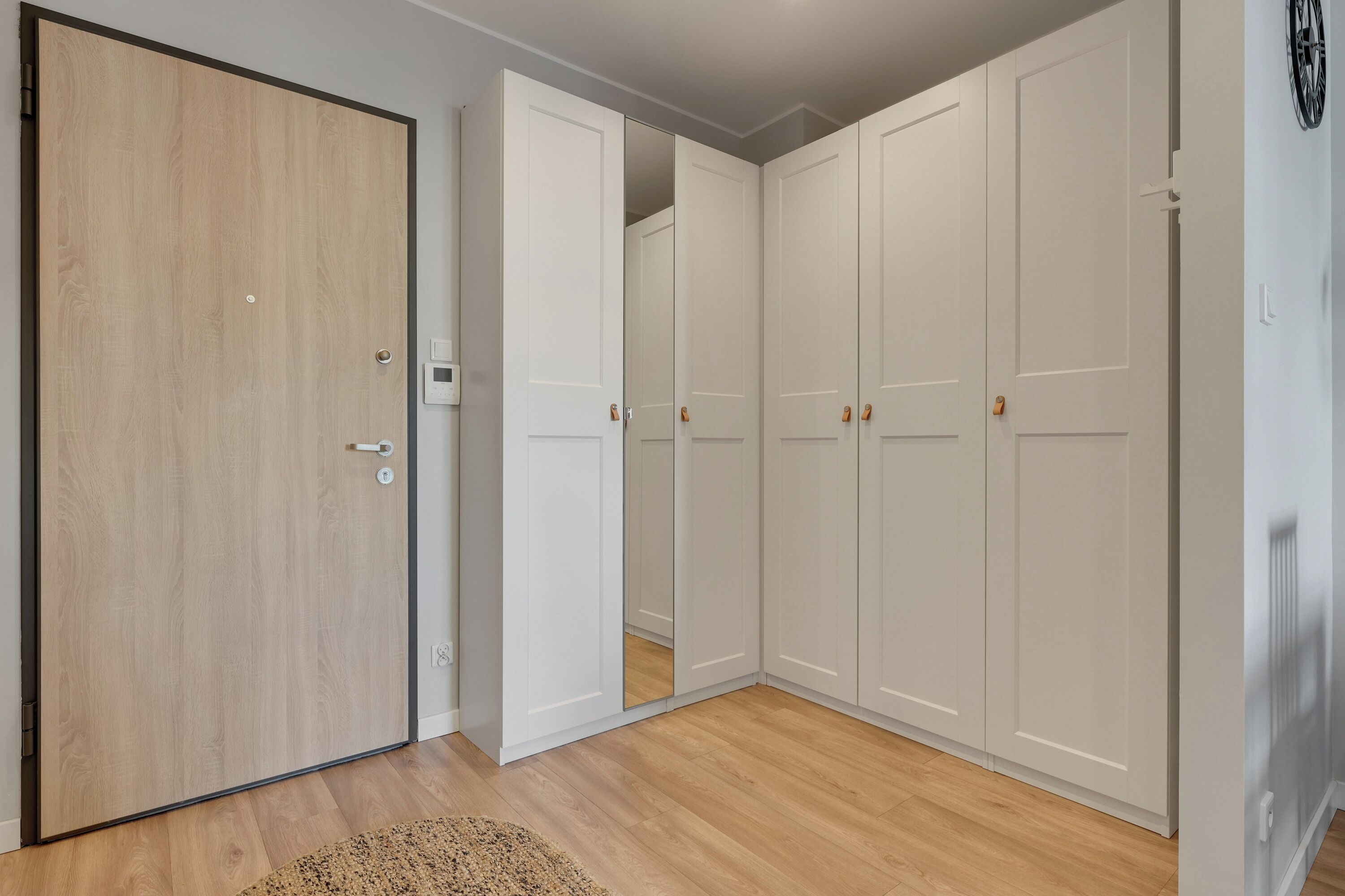 A room with a wooden door, white wardrobes, and a light-colored carpet.