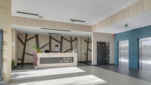 A reception desk with 'NOWA LETNICA' signage, a modern interior with geometric wall patterns, and a clean, spacious lobby area. - Letnica 31 by Grand Apartments (Gdańsk)