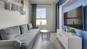 A modern living room with a grey sofa, a round coffee table, a flat-screen TV, and a white cabinet. - Letnica 31 by Grand Apartments (Gdańsk)