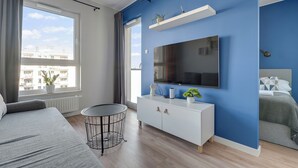 A modern bedroom with a large window, a flat-screen TV, a white dresser, and a bed with a grey blanket. - Letnica 31 by Grand Apartments (Gdańsk)