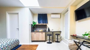 Uma cozinha compacta com fogão embutido, dois bancos de bar, bancada pequena e TV fixada na parede.