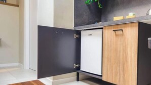 Uma cozinha compacta com geladeira embutida, um armário de madeira e bancada preta.