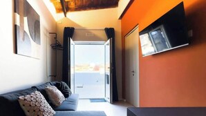 A room with a sofa, a TV mounted on the wall, and a door leading to an outdoor area. - Vesuvio | Penthouse Pignasecca – Design Suite (Naples)