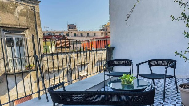 A balcony with a table and chairs, a potted plant, and a view of neighboring buildings. - Vesuvio | Penthouse Pignasecca – Design Suite (Naples)