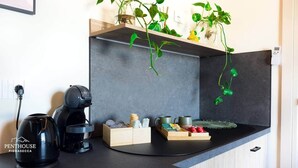 A kitchen with a coffee maker, a kettle, and a shelf with plants and kitchenware. - Vesuvio | Penthouse Pignasecca – Design Suite (Naples)