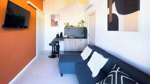 A compact living space with a kitchenette, a sofa, a TV, and artwork on the walls. - Vesuvio | Penthouse Pignasecca – Design Suite (Naples)