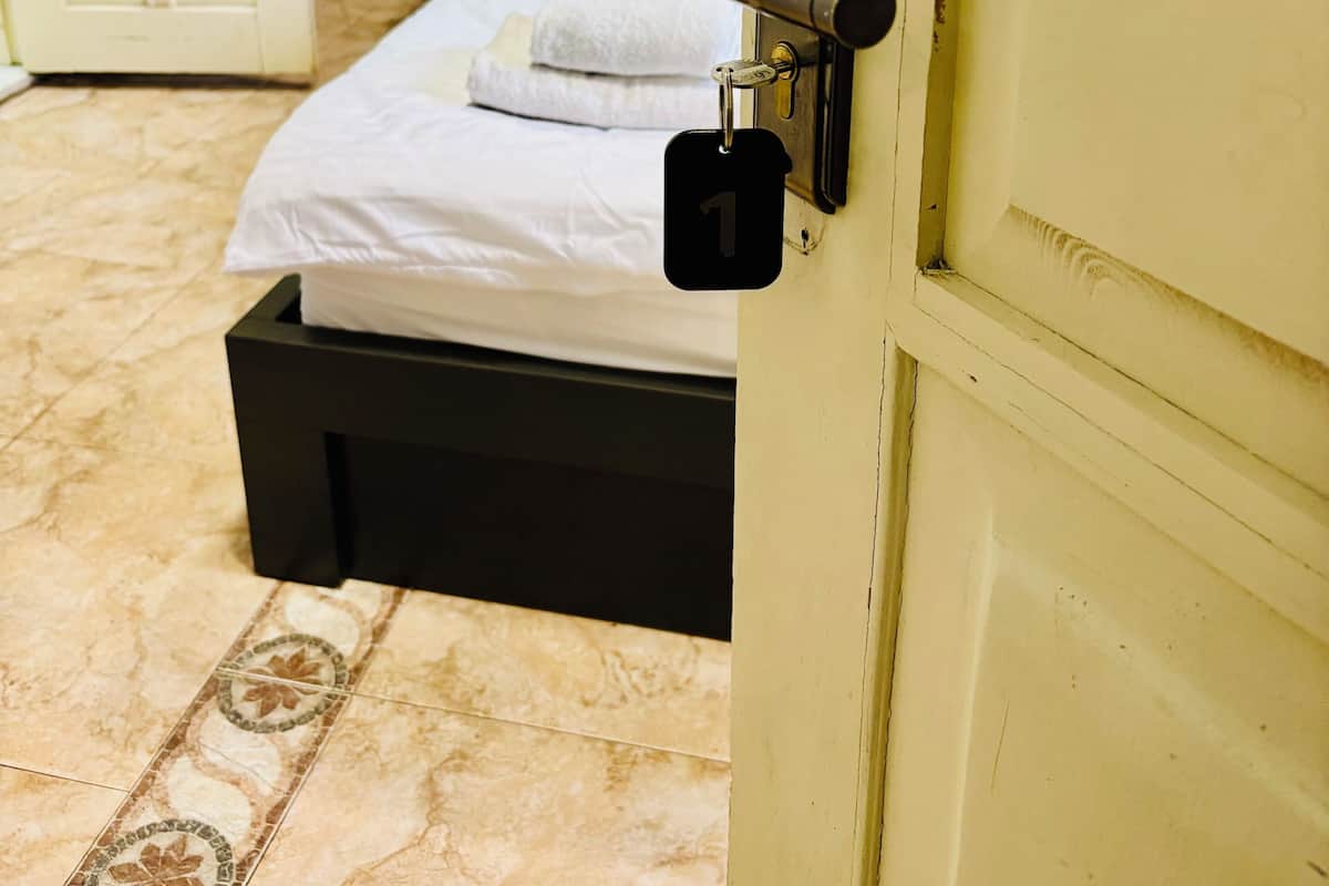 A hotel room with a bed, a bedside table, a lamp, and a door with a lock.