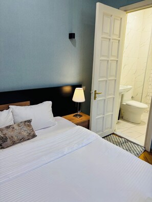 A hotel room with a bed, a nightstand with a lamp, and an open door to a bathroom with a toilet and sink. - 62 Dimitri Uznadze str. (Tbilisi)