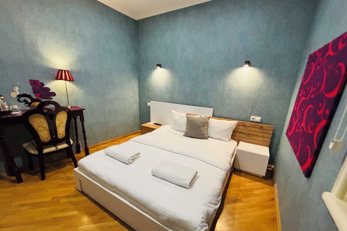A bedroom with a bed, bedside tables, a desk, and a chair.