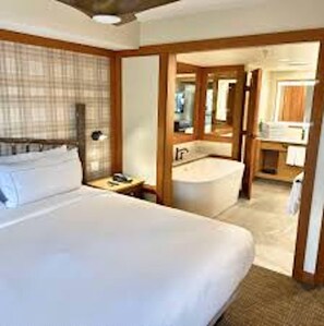 Ein Hotelzimmer mit einem großen Bett, einem Badezimmer mit einer Badewanne und einem Schreibtisch mit einem Stuhl.