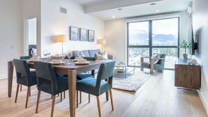Un espace repas moderne avec une table en bois, des chaises foncées et une grande fenêtre donnant sur une vue imprenable sur les montagnes.