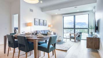 A modern dining area with a wooden table, dark chairs, and a large window offering a mountain view.