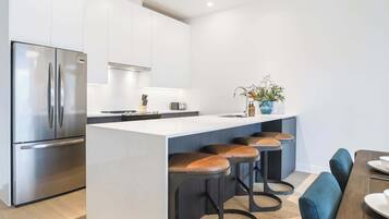 A modern kitchen with a stainless steel refrigerator, a central island with stools, and a dining area with a table and chairs.