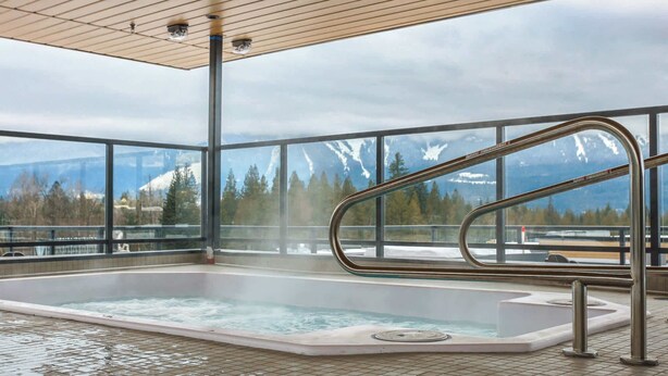Un bain à remous avec vue sur des montagnes enneigées, un plafond en bois et une rambarde en métal.