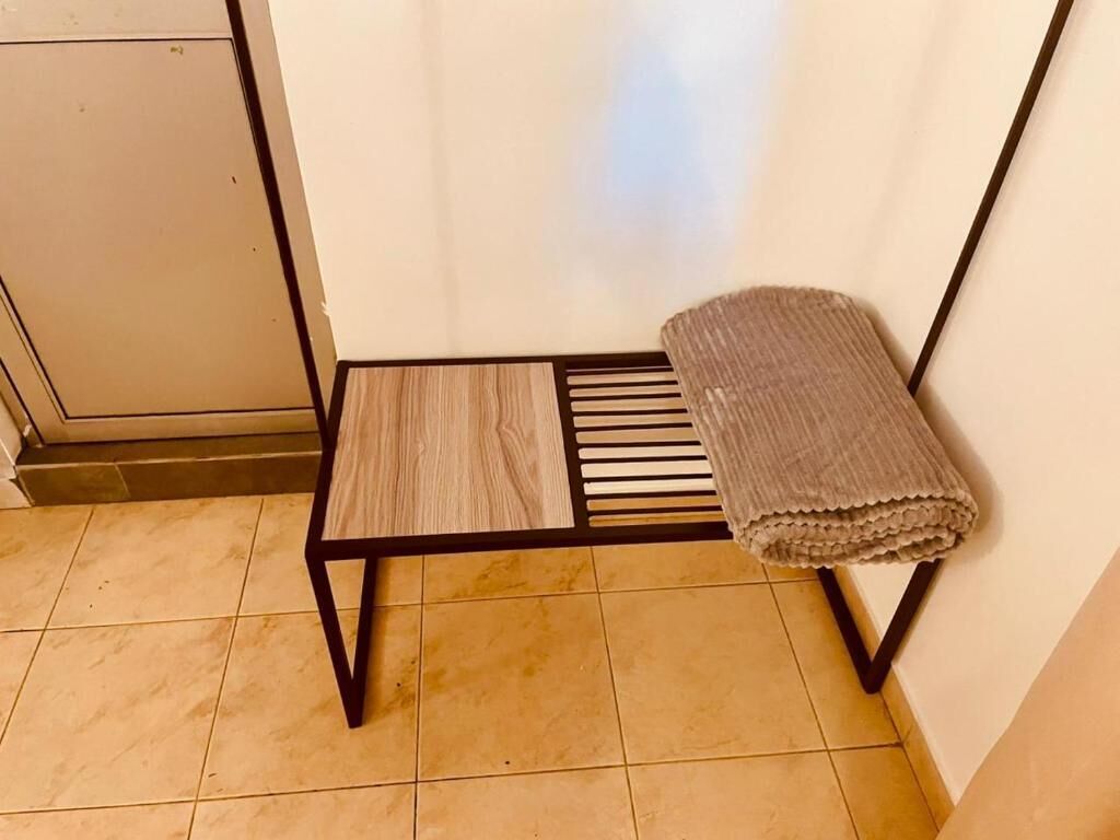 Een kleine, eenvoudige kamer met een bankje, een radiator en een wandplank.